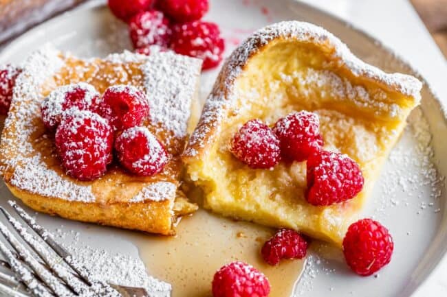 two pieces of German pancakes on a plate with raspberries.