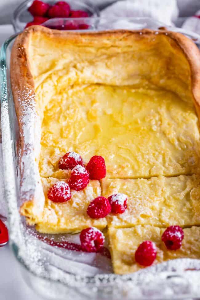 puffy pancakes in a 9x13 pan with raspberries and powdered sugar.