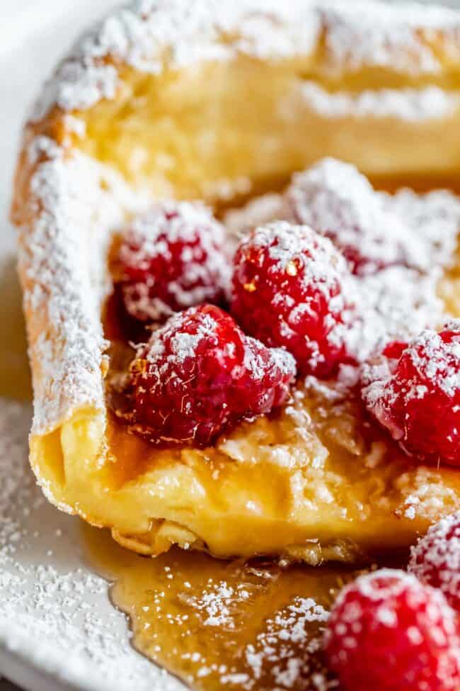 dutch baby with raspberries, syrup, and powdered sugar.