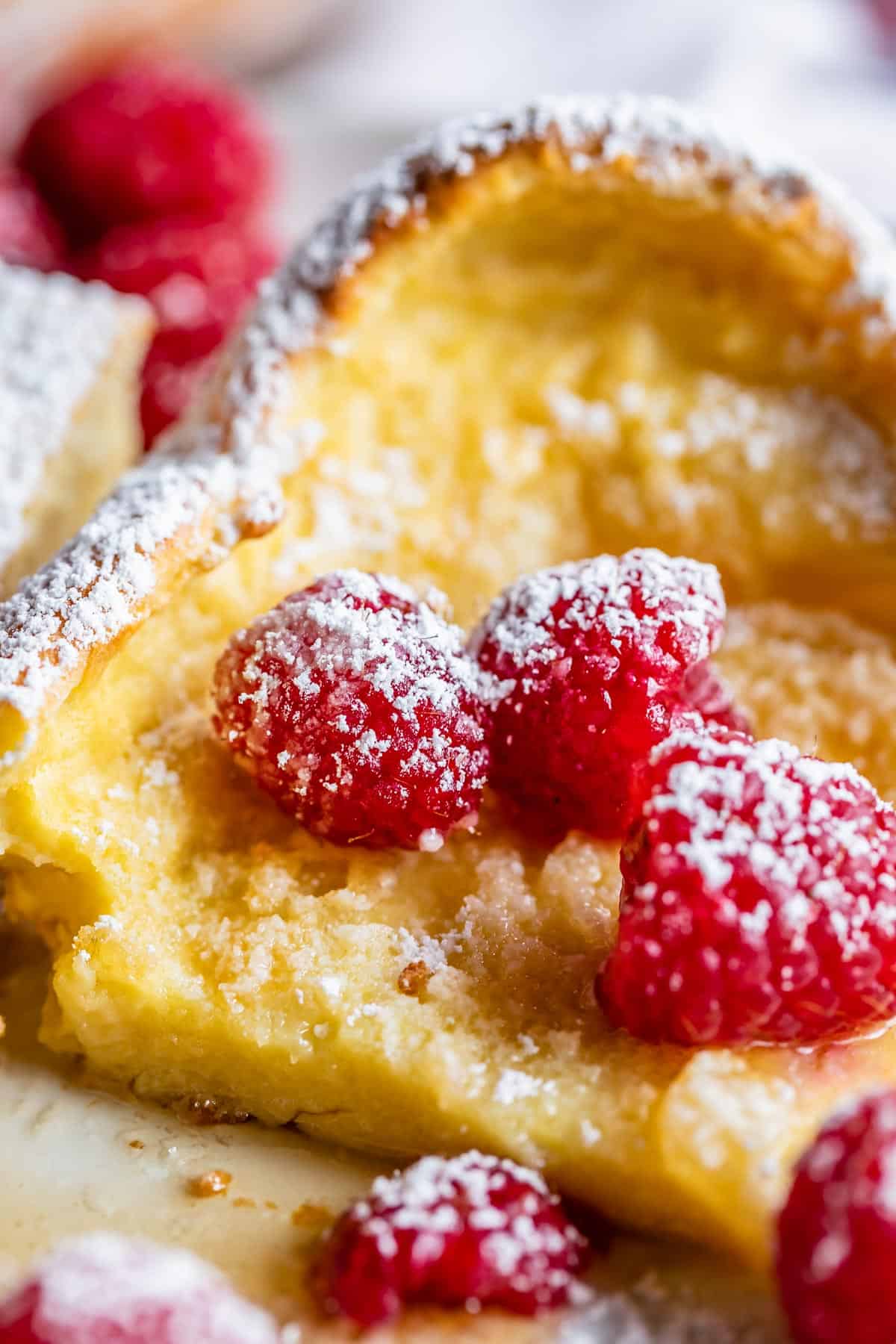 puffy pancakes on a plate with raspberries and powdered sugar.