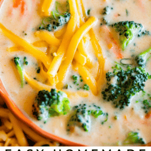 Close-up of a bowl of creamy broccoli cheese soup topped with shredded cheddar cheese, with visible pieces of broccoli and carrots. Text overlay reads Easy Homemade Broccoli Cheese Soup - The Food Charlatan, featuring a rich, cheesy flavor.