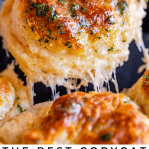 A close-up of golden, cheesy cheddar bay biscuits topped with herbs. One biscuit is being lifted, revealing gooey, melted cheese stretching. Text at the bottom reads: Copycat Cheddar Bay Biscuits - The Food Charlatan.