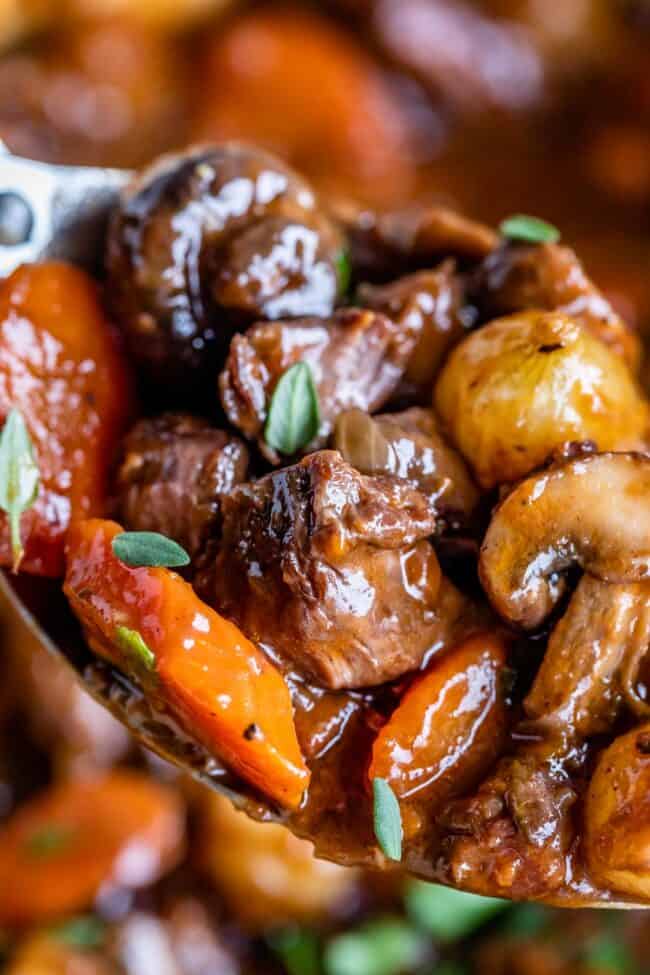 close up of beef, carrots, mushrooms, pearl onions, and parsley on a spoon.