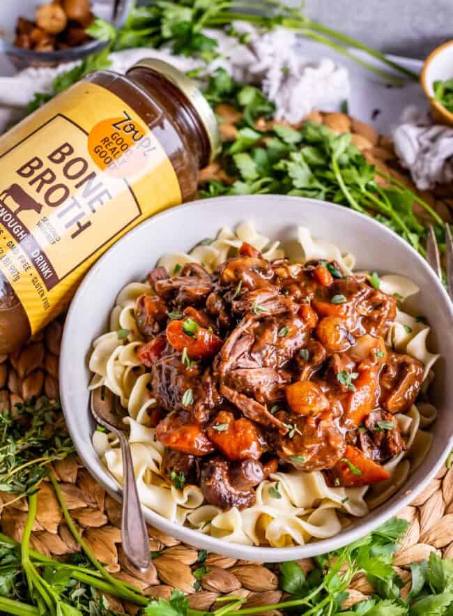 a bowl of egg noodles topped with Julia Child's beef bourguignon, next to a jar of Zoup! Broth