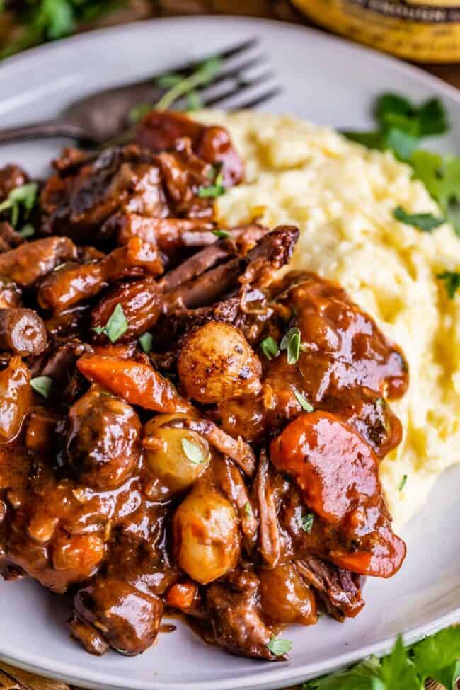 beef bourguignon stew on a plate next to mashed potatoes, with a fork in the background