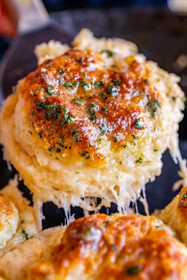 lifting a cheddar biscuit from a cast iron pan with cheese stretch.