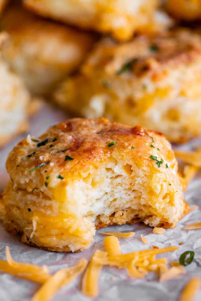 cheddar biscuit on parchment paper, with shredded cheddar cheese in the foreground.