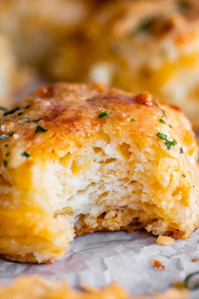 a bite taken out of a cheddar bay biscuit sitting on parchment paper.