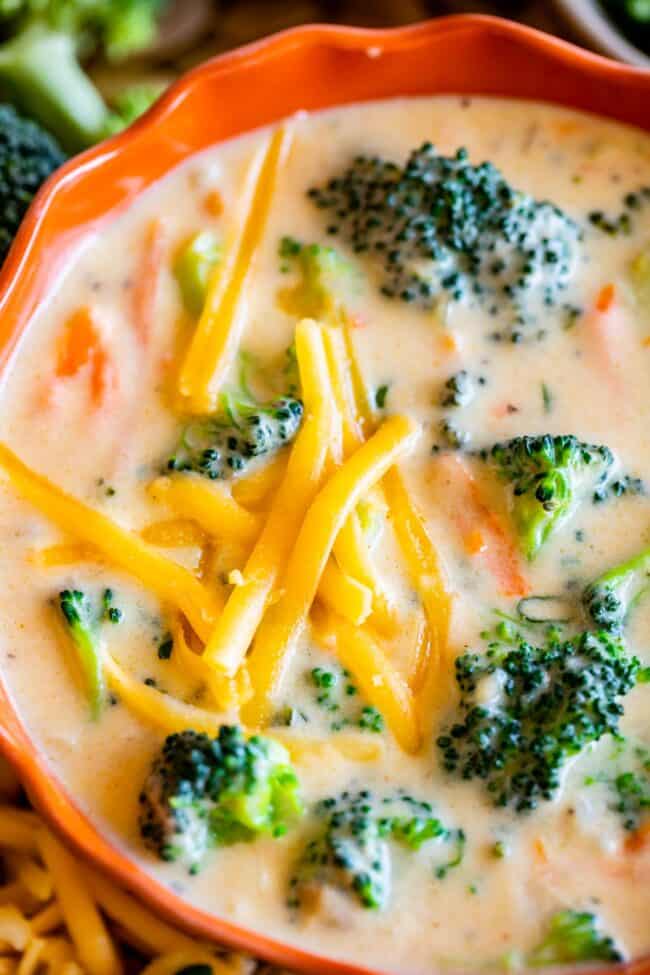 overhead shot of broccoli cheese soup in an orange bowl, sprinkled with cheddar cheese.