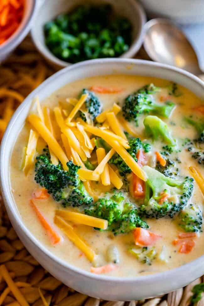 broccoli and cheese soup in a white bowl with green onions in a bowl in the background.