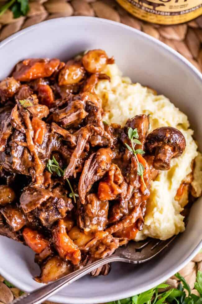 beef bourguignon in a white bowl with mashed potatoes and a fork.