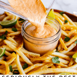 A blender pours creamy orange chipotle mayonnaise into a small jar, surrounded by French fries garnished with lime wedges and cilantro. Text below reads, Seriously flavorful Chipotle Mayonnaise to put on everything.