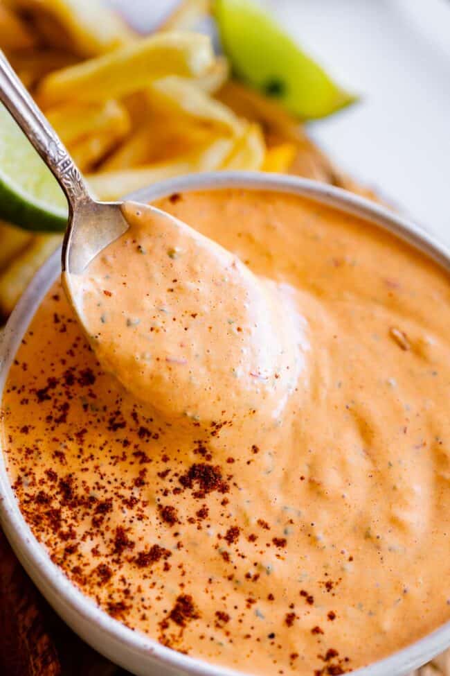 spoon lifting chipotle mayo recipe from a bowl sprinkled with chipotle powder