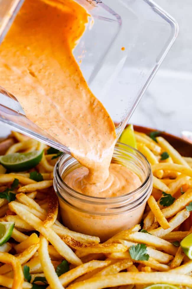pouring chipotle mayo sauce into a mason jar surrounded by fries