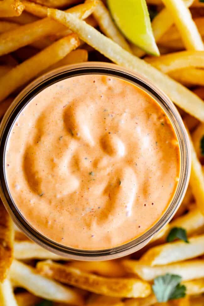 close up of chipotle mayo sauce in a mason jar, with french fries and lime slices.