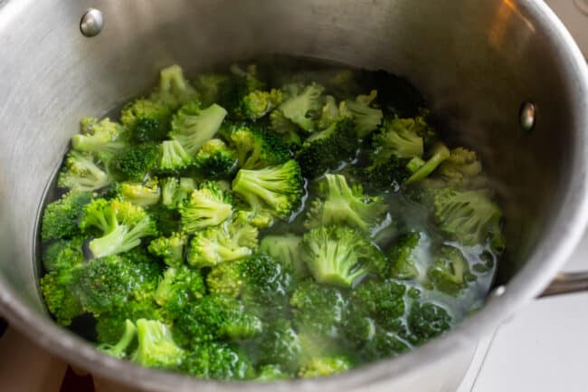 broccoli being blanched in water in a large silver pot.