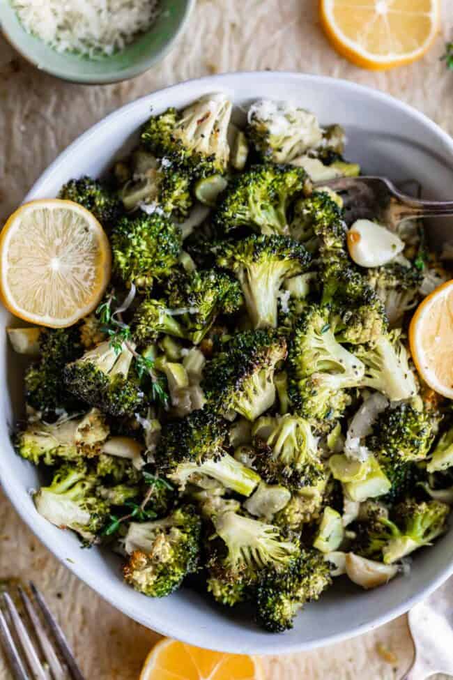 roasted broccoli in a white bowl with lemons on the side.