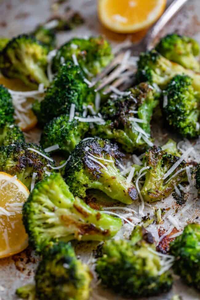 roasted broccoli recipe, sprinkled with parmesan with lemons and fork in the background.
