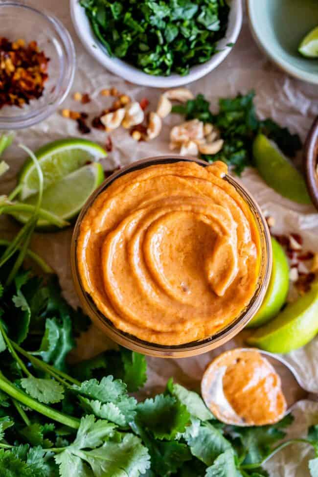 spicy thai peanut sauce in a jar surrounded by limes, cilantro, crushed peanuts