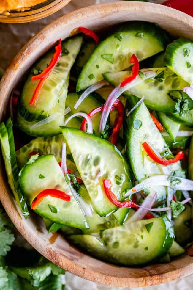 thai cucumber salad with cucumbers, shallots, red pepper, and cilantro in a wooden bowl.