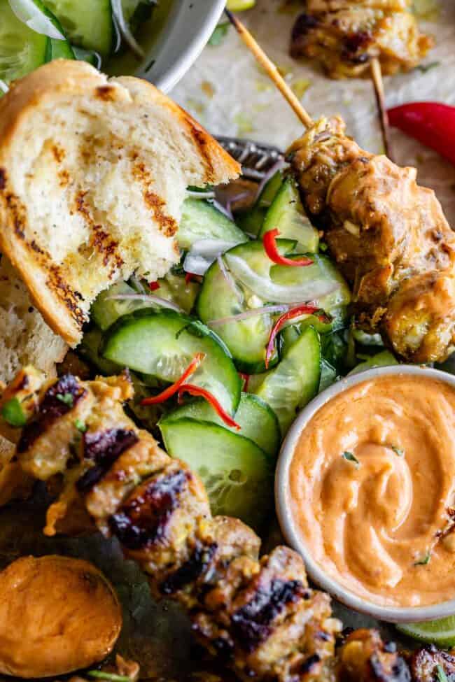 thai inspired chicken satay, peanut sauce, cucumber salad, and bread on a plate.