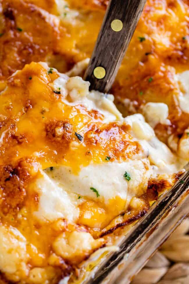 scalloped potatoes with cheese being lifted out of the pan with a spatula