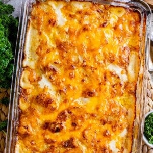 cheesy scalloped potatoes in a glass casserole dish with a tan napkin and parsley