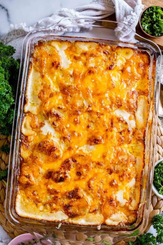 cheesy scalloped potatoes in a glass casserole dish with a tan napkin and parsley