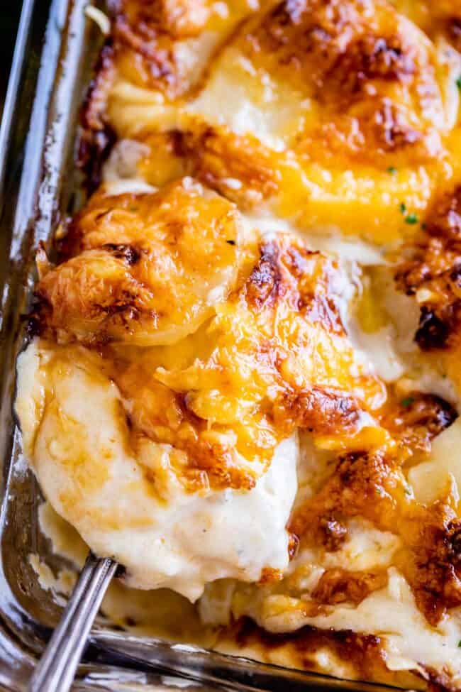 cheesy scalloped potatoes in a casserole dish with a spoon lifting some out.