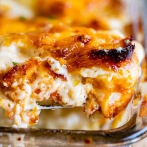 scalloped potatoes with crispy edges being lifted from a clear casserole dish
