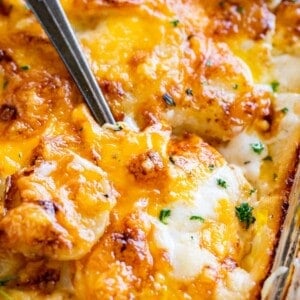 cheesy scalloped potato recipe in a pan, shot from overhead with a spoon