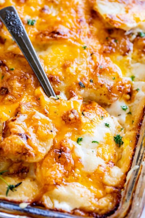 cheesy scalloped potato recipe in a pan, shot from overhead with a spoon