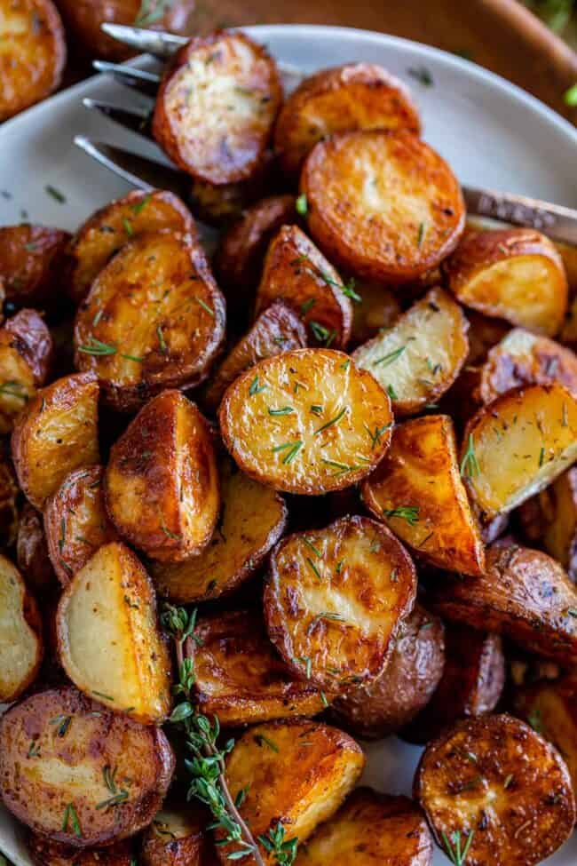 roasted red potatoes with fresh thyme on a white plate with a fork.