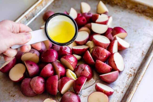 adding oil to red potatoes on a sheet pan.
