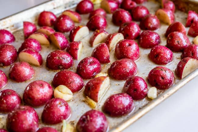 red potatoes tossed with oil and garlic and arranged cut side down on a sheet pan.