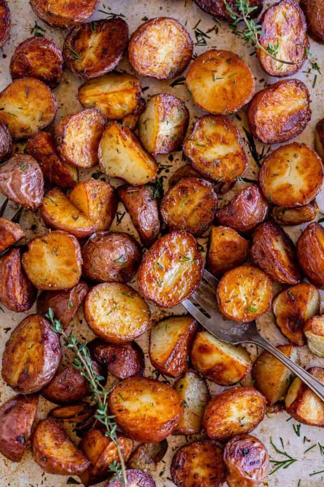 roasted red potatoes with fresh thyme on a sheet pan with a fork.