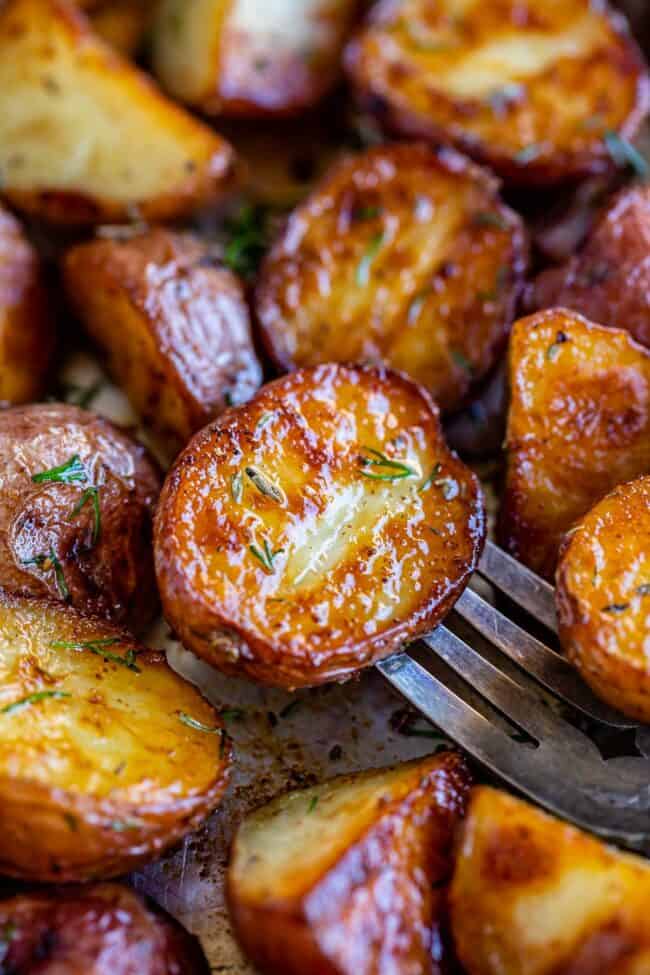 roasted red baby potatoes on a pan with herbs, one pierced with a fork.