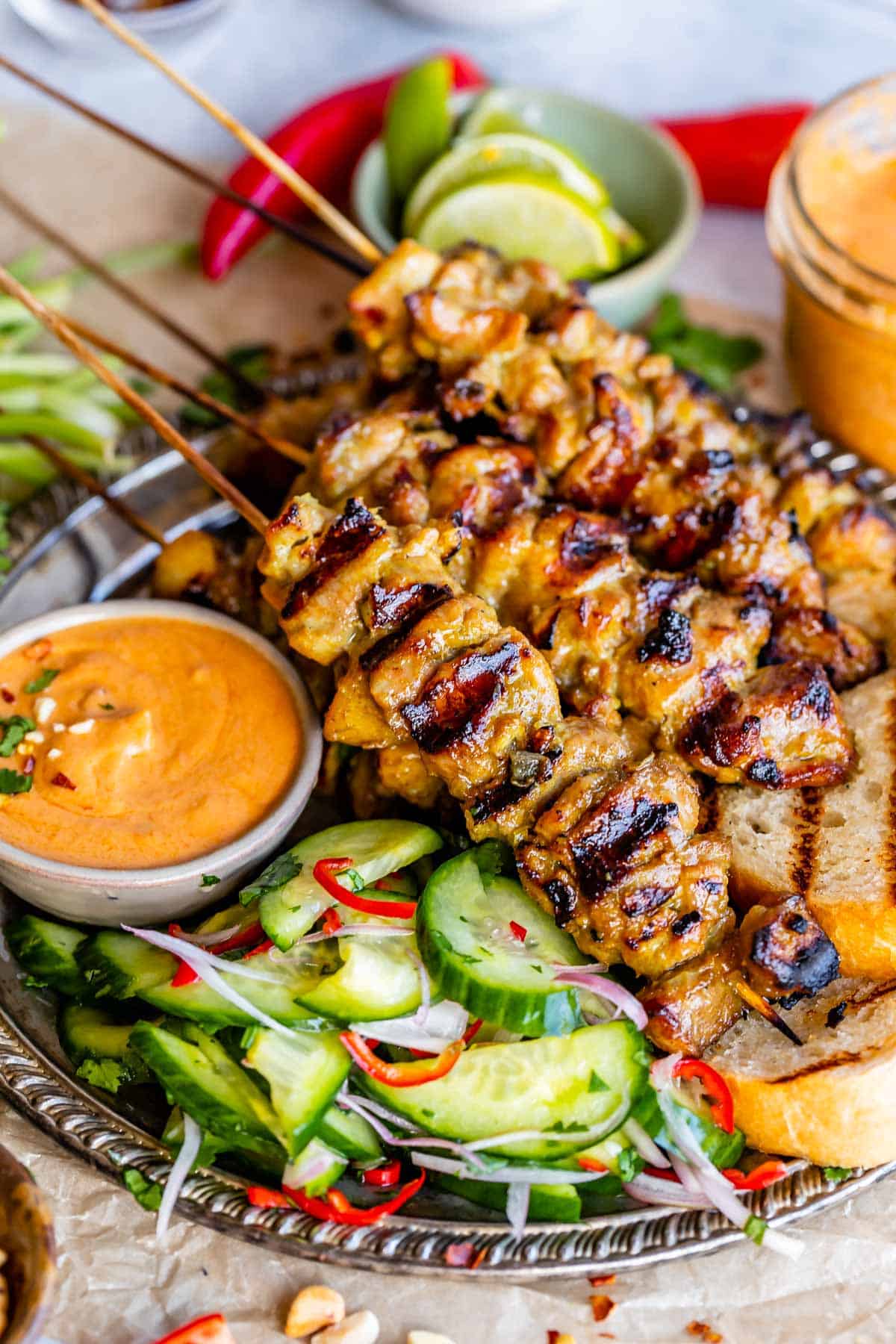 chicken satay sauce in a bowl next to chicken on a silver plate with cucumber salad.