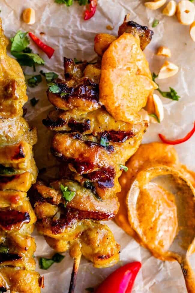 chicken satay on skewers with a spoonful of peanut sauce.