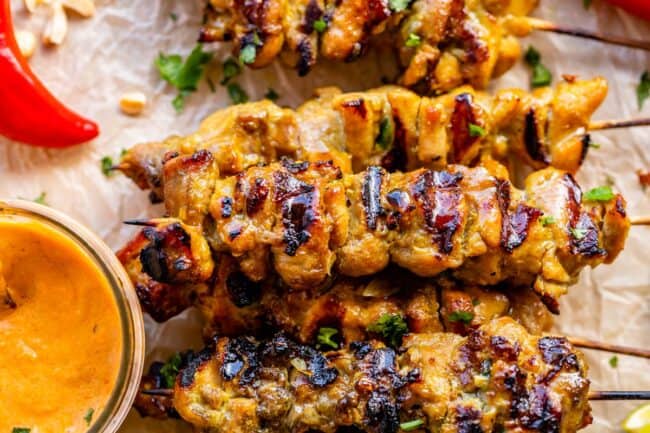 chicken satay skewers lined up next to a bowl of peanut sauce.
