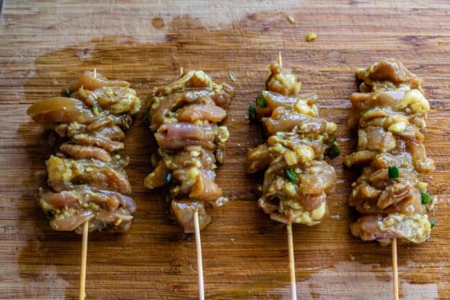 marinated chicken pieces threaded onto wooden skewers on a wooden cutting board.