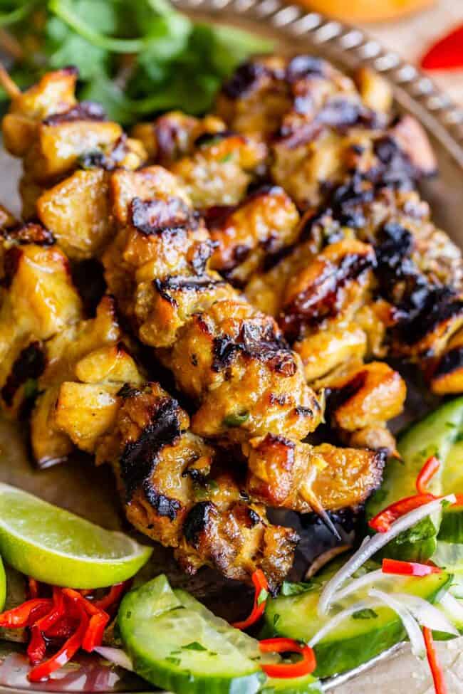 chicken satay recipe on a sliver plate with cucumber salad.