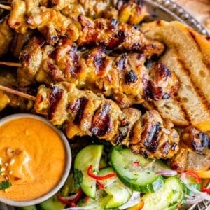 chicken satay with peanut sauce in a bowl as well as cucumber salad