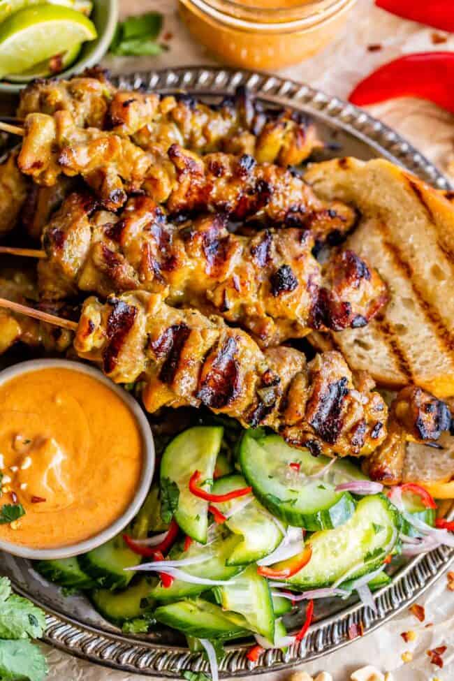 chicken satay with peanut sauce in a bowl, cucumber salad, and grilled bread.