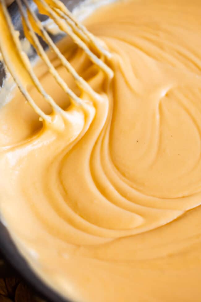 Swirling a whisk through a pan of cheese sauce.