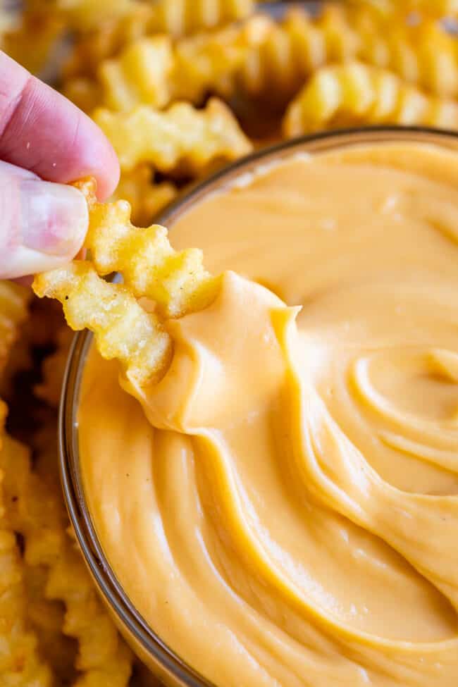 easy cheese sauce in a bowl with a hand dipping two french fries