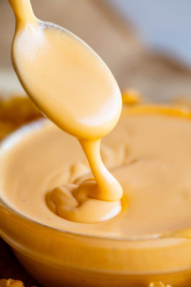 a spoon drizzling homemade cheese sauce into a clear bowl.