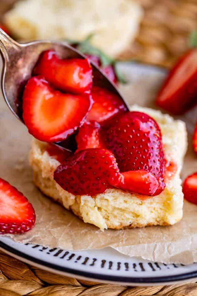 spooning strawberries onto shortcake on a plate.