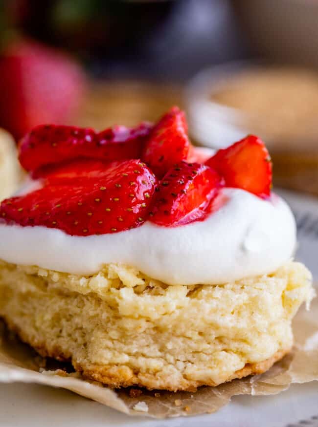 shortcake on parchment paper topped with whipped cream and strawberries.