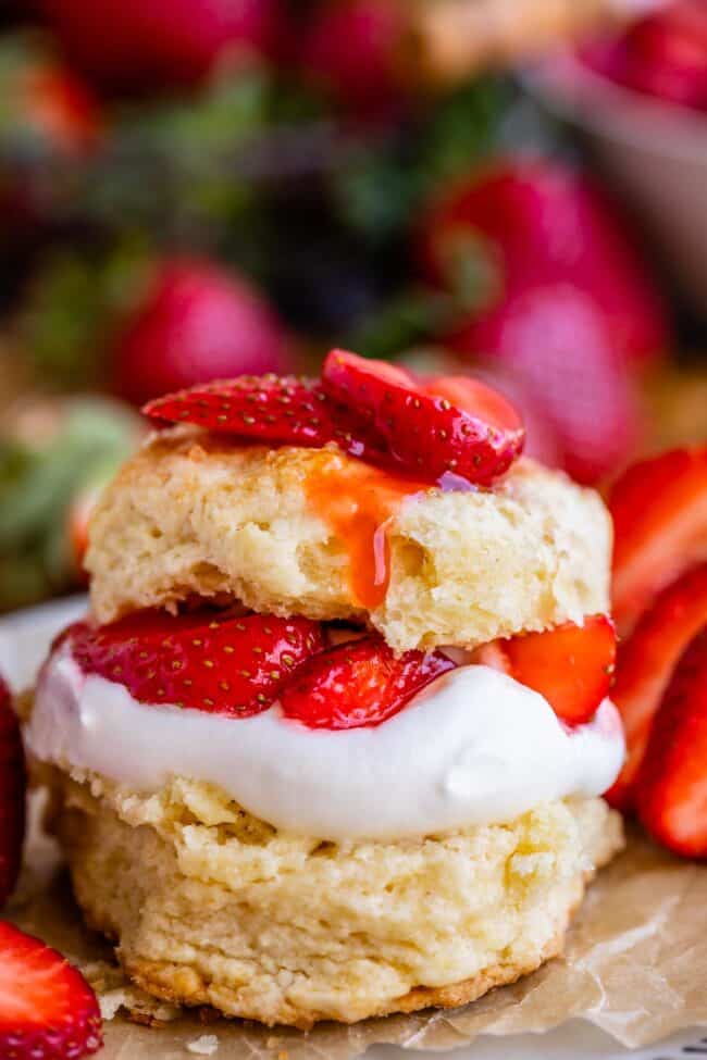 strawberry shortcake stacked on parchment paper on a plate with strawberries in the background.